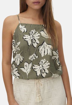 Femme portant un haut sans manches vert olive avec un imprimé floral blanc, associé à un pantalon crème texturé noué avec une ceinture en corde.