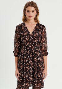 Robe noire à fleurs en tissu léger, avec un décolleté en V, des manches transparentes trois-quarts et une taille élastique avec une jupe fluide.