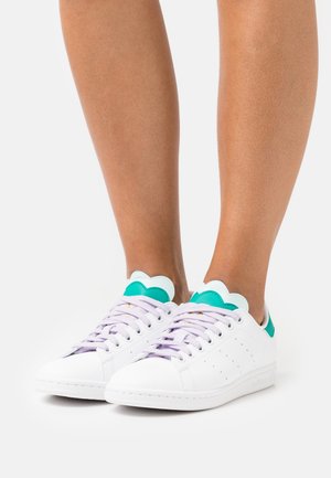 Sneakers bianchi con finitura in pelle liscia, lacci lavanda e dettagli scallop teal sul tallone. Presentano un motivo perforato sui lati.