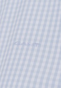 Light blue and white gingham patterned fabric with a smooth texture, featuring embroidered "GANT" logo at the bottom.