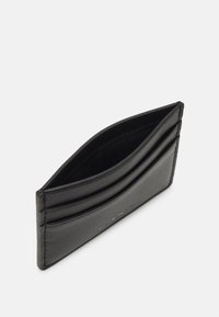 Cardholder din piele neagră, cu patru sloturi, un design elegant și textură netedă. Are margini arcuite și detalii subtile cu logo embosat.