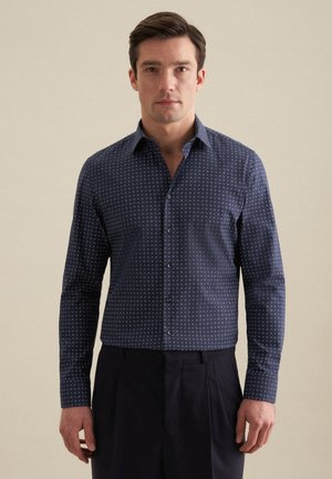 Camicetta blu navy con bottoni realizzata in un tessuto testurizzato con un motivo geometrico ripetuto di piccole dimensioni. Presenta un colletto e maniche lunghe.