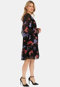 Czarna przezroczysta sukienka z kwiatowym wzorem w czerwieni i niebieskim. Posiada długie rękawy w kształcie dzwonu, falbany u dołu i koronkowe wykończenia przy mankietach. Połączona z czarnymi szpilkami.