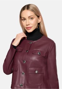 Bordowa skórzana kurtka z okrągłym dekoltem, srebrnymi guzikami i dwoma kieszeniami na piersi. Gładka tekstura i dopasowany krój.