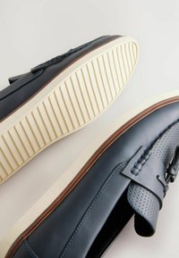 Zapatos de cuero tipo mocasín en azul medianoche con un detalle texturizado en la parte superior, suela blanca con estrías y ribete marrón alrededor de la suela.