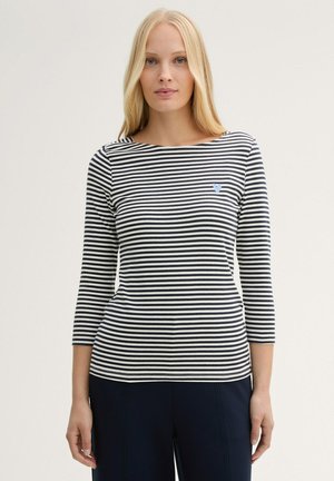 T-shirt à manches longues rayé, avec des rayures horizontales bleu marine et blanches, doté d'un col rond et d'un petit emblème en forme de cœur bleu sur la poitrine gauche.