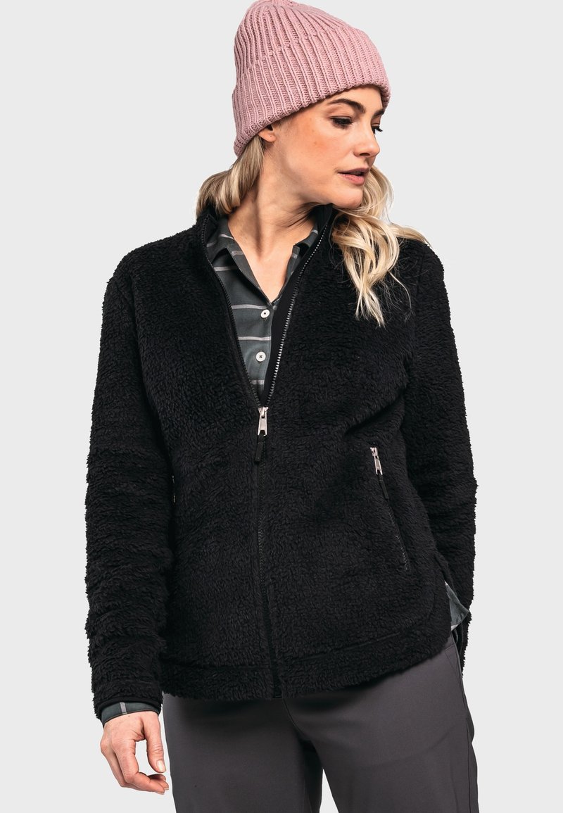Schwarze Fleecejacke mit Reißverschluss, seitlichen Taschen und strukturiertem Stoff. Über einem karierten Hemd getragen, kombiniert mit einer hellrosa Mütze.