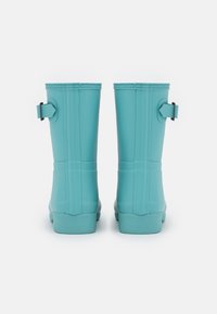 Botas de lluvia de goma turquesa con un acabado suave, diseño erguido y acentos de hebilla lateral. La suela es ligeramente texturizada para proporcionar tracción.
