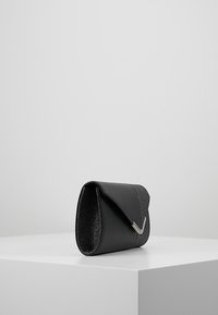 Černé psaníčko s matným koženým tělem a třpytivým horním klopou. Na přední straně stříbrný zvýrazňující prvek ve tvaru písmene V. Krabicovitý tvar, minimalistický design.