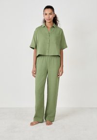 Completo di colore verde chiaro composto da una camicia a maniche corte con bottoni e pantaloni larghi in tessuto strutturato.