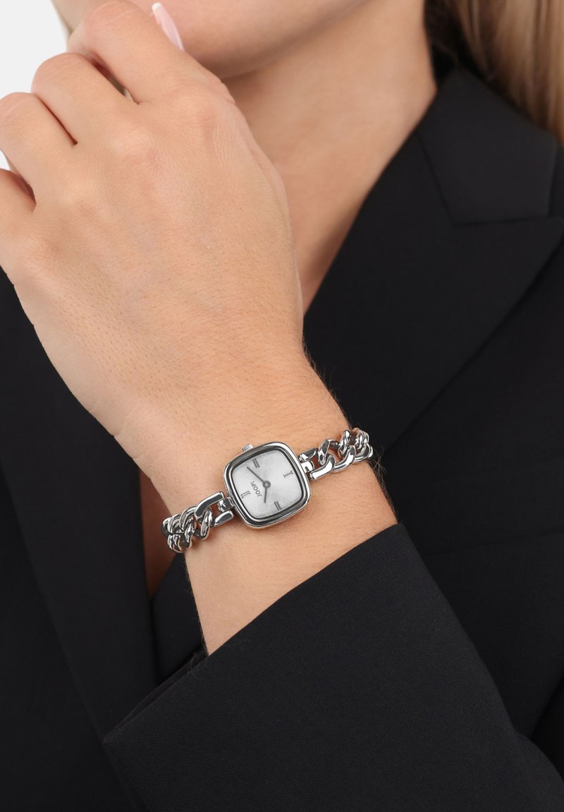 Zilverkleurig horloge met een vierkante wijzerplaat, zwarte wijzers en een schakelarmband. Het horloge heeft een minimalistisch ontwerp en een metalen glans.