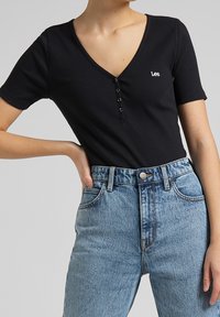 Sort ribbetop med korte ærmer, V-hals og knaplukning. Sammen med højhalsede lyseblå denim jeans med et logo-knap.