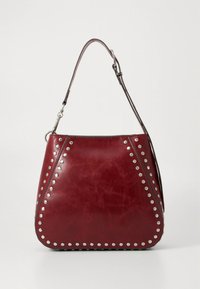 Sac à main en cuir rouge avec une forme incurvée, présentant des clous argentés le long des coutures et une seule bandoulière réglable.