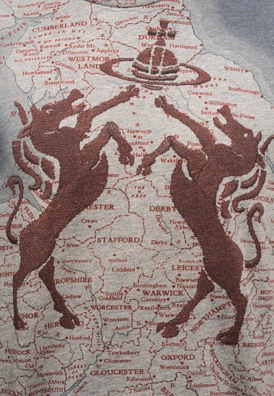 Γκρι ύφασμα με λεπτομερή κόκκινο σχέδιο χάρτη που περιλαμβάνει ετικέτες κειμένου με αγγλικές τοποθεσίες. Δύο καφέ κεντημένα μονόκεροι εμφανίζονται κυρίαρχα.