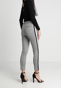 Šedé zúžené kalhoty s jemnou texturou mají boční proužek v námořnické modři a bílé. V kombinaci s černými stiletto podpatky a černým topem.