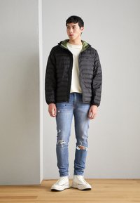 Geacă puf negre cu glugă verde, asortată cu blugi deschiși, deteriorați, de culoare albastră și adidași albi. Textură netedă, design casual.