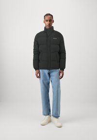 Sort puffer-jakke med høj krave, quiltet tekstur og lynlås lukning. Båret med lyseblå jeans og cremefarvede sneakers.
