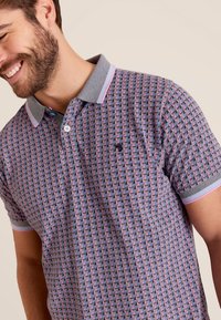 Polo shirt in een geometrisch patroon met roze, blauw en zwarte kleuren; voorzien van een grijze kraag met contrasterende strepen en twee knopen.