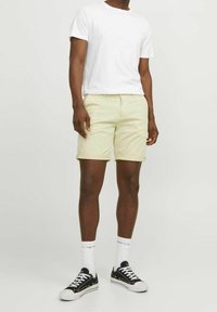 Světle žluté šortky s ohrnutými lemy, se zipem a předními kapsami, spárované s obyčejným bílým tričkem a černými teniskami.