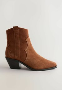 Botas de ante marrón hasta el tobillo con puntera afilada, costuras laterales curvadas y tacón cuadrado. Diseño simple con sutiles acentos en textura.