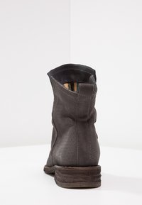 Bottine en cuir noir avec design perforé, un bout légèrement arrondi et un talon bas empilé. L'intérieur est doublé de tissu doux.
