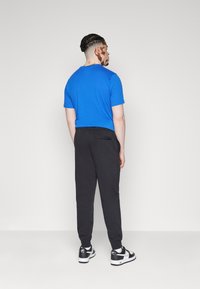 T-shirt di cotone blu abbinato a pantaloni della tuta neri. Tessuto morbido; vestibilità casual. Sneakers bianco e nere completano il look.