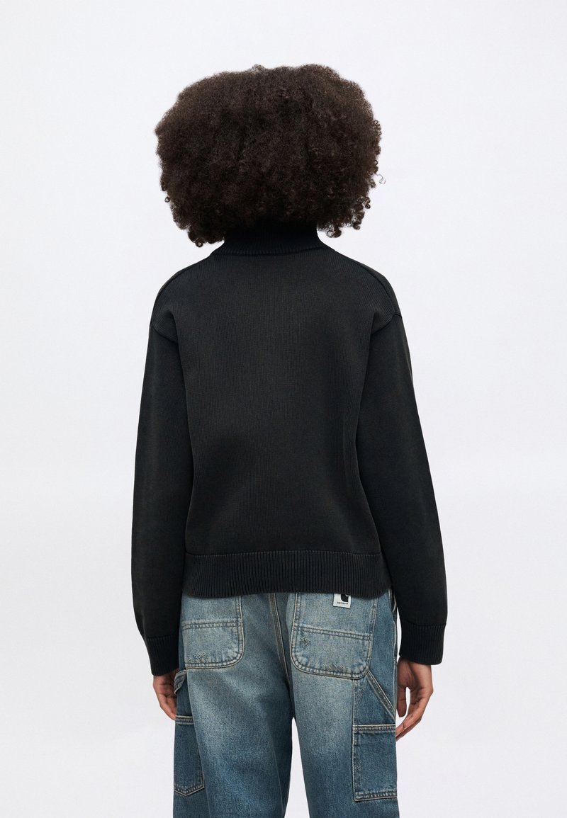 Black ribbed sweater with high collar, cropped length, and flexible fit, paired with light blue cargo jeans featuring utility pockets.