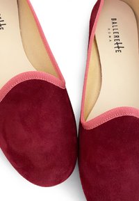Ballet flats en daim rouge avec un bout arrondi et un contour rose contrastant sur les bords. Doublure intérieure lisse avec la marque "Ballerette Roma" visible à l'intérieur.
