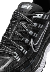 Juodas Nike sportbaikis su tinklinėmis viršutinėmis dalimis, sidabriniais akcentais, sudėtinga raištelių sistema ir paminkštintu padu su tekstūruota paviršiaus danga.