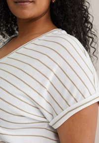 Top bianco con strisce orizzontali beige, con maniche corte e scollo a V. Il tessuto appare morbido e leggero con una trama liscia.