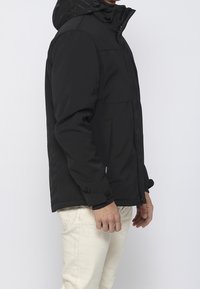 Veste noire isolante avec capuche, dotée d'une fermeture éclair devant, de poignets élastiques et de poches latérales. Tissu lisse avec des détails de coutures minimales.