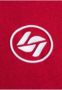Roter Stoff mit einem weißen, gestickten, kreisförmigen Logo, das stilisierte Buchstaben im Inneren zeigt und Textur sowie dreidimensionale Details hervorhebt.