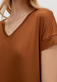 Braunes V-Ausschnitt-Oberteil mit kurzen Ärmeln, aus glattem Stoff gefertigt; mit einem aufgerollten Ärmel-Detail und einer lockeren Passform.