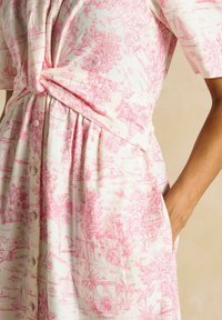 Ceļgala garuma kleita mīkstā audumā, ar rozā toile drukāšanu, kas attēlo ainavas un laivas, ar sasietu jostas vietu un sānu kabatām.