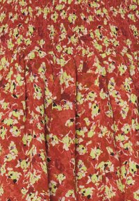 Robe florale rouge avec un corsage smocké et une jupe plissée. Motifs jaunes et noirs sur un tissu texturé.