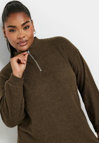 Maglione marrone a coste con zip a metà e maniche lunghe, dotato di colletto alto. Presenta una chiusura lampo in metallo argentato e un tessuto texturizzato.