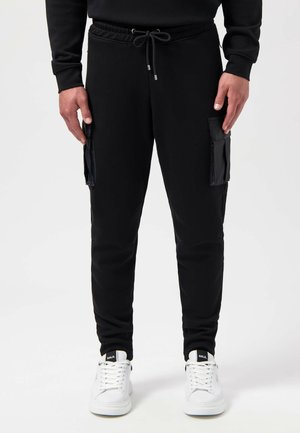 Black jogger pants with a drawstring waist, side cargo pockets, tapered legs, and elastic cuffs, paired with white sneakers.