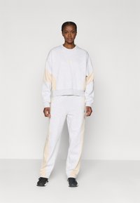 Γκρι φούτερ με μπεζ πλαϊνές ρίγες και έναν μικρό λογότυπο στο στήθος, συνδυασμένο με γκρι φόρμες και μαύρα αθλητικά παπούτσια.