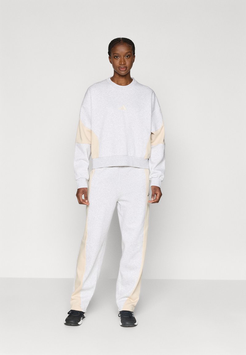 Γκρι φούτερ με μπεζ πλαϊνές ρίγες και έναν μικρό λογότυπο στο στήθος, συνδυασμένο με γκρι φόρμες και μαύρα αθλητικά παπούτσια.