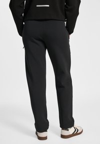 Pantalons de survêtement noirs avec une coupe décontractée, dotés de poches latérales et de bords côtelés. Portés avec des baskets beiges et noires. Texture de tissu lisse.