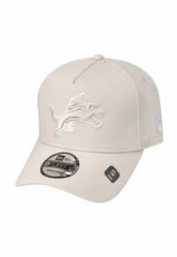 Verstellbare beige Kappe mit strukturiertem Oberflächen, versehen mit einem weißen gestickten Löwenlogo auf der Vorderseite und einem schwarzen runden Etikett auf dem Schirm.
