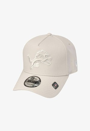 Casquette beige réglable avec une surface texturée, affichant un logo de lion brodé blanc à l'avant et une étiquette circulaire noire sur la visière.