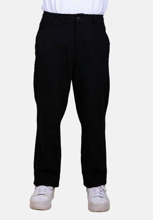 Pantalones negros de pierna recta con cintura elástica y cierre de botón, usados con zapatillas blancas y una camiseta blanca.