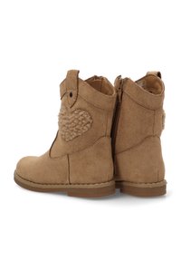 Botas de tobillo de ante color beige con un acento texturizado en forma de corazón en el lateral, cierre de cremallera y suelas de goma planas. Presenta detalles de costura.