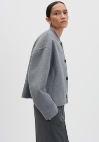 Veste grise courte en laine douce, avec un col rond, des manches oversize et des boutons noirs pour la fermeture.