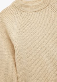 Beżowy sweter dzianinowy z teksturowanym wzorem, z wysokim kołnierzem i rękawami raglanowymi. Materiał wydaje się miękki i przytulny.