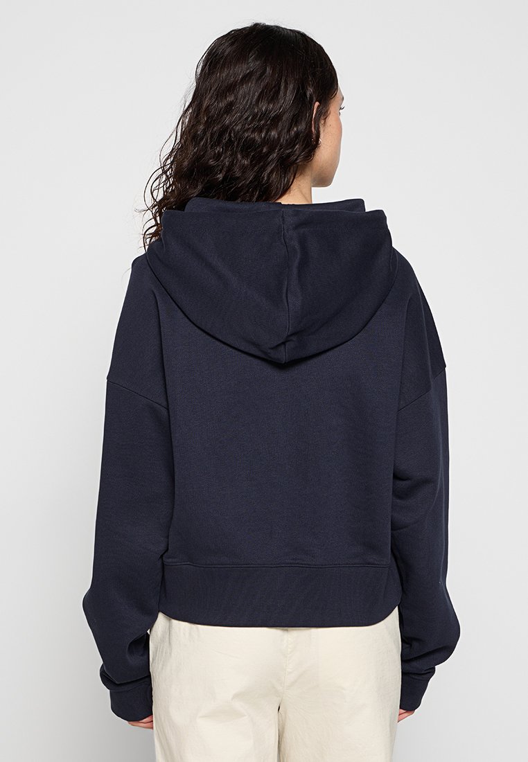 Granatowa krótka bluza z kapturem na sznurku, szerokimi rękawami i ściągaczem u dołu. Miękka tekstura z minimalną ilością szwów, zaprojektowana z myślą o luźnym kroju.