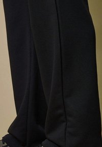 Pantalons noirs ajustés portés avec des baskets noires, montrant en gros plan la texture du tissu et les lignes de couture.