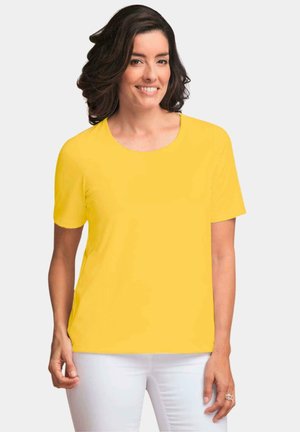 T-shirt giallo a maniche corte in un tessuto liscio e leggero con scollatura rotonda, abbinato a pantaloni bianchi. Design semplice e a tinta unita.