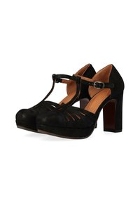 Scarpe nere in suede con tacco alto, design a T-straps, dettagli intagliati e punta chiusa. I tacchi sono robusti e alti circa 12,5 centimetri.